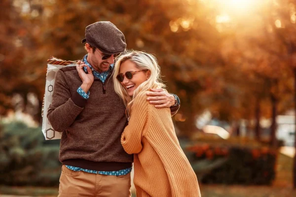 Coppia sorridente che si abbraccia all'aperto in una giornata autunnale.